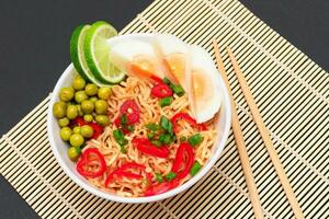 Beautiful Noodle Dish with Green Pea, Eggs, Red Hot Pepper, Greens and Lime with Chopsticks on Sushi Mat. Instant Noodles photo