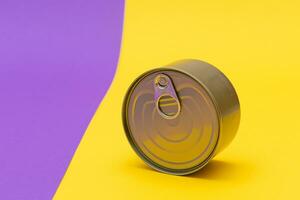 Unopened Tin Can with Blank Edge on Split Yellow and Violet Background. Canned Food. Aluminum Can for Safe and Long Term Storage of Food. Steel Sealed Food Storage Container photo