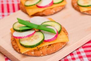Light Breakfast. Quick and Healthy Sandwich. Fresh Cucumber and Radish with Green Onions and Cheese on Crispy Cracker on Wooden Cutting Board photo
