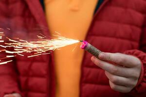 joven hombre Encendiendo arriba petardo en su mano al aire libre. chico consiguiendo Listo para nuevo año divertido con fuegos artificiales o pirotécnico productos de cerca Disparo foto