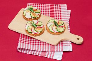 Light Breakfast or Diet Eating Crispy Cracker Sandwich with Cream Cheese, Fresh Cucumber and Radish on Wooden Cooking Board on Magenta Background photo