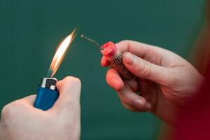 Man Lighting Up Firecracker in his Hand Against the Blue Background Using Gas Lighter photo