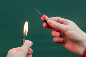 Man Lighting Up Firecracker in his Hand Against the Blue Background Using Gas Lighter photo