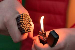 Man in Red Jacked Lighting Up Many Small Black Firecrackers in his Hand Using Gasoline Lighter. Guy Getting Ready for New Year Fun with Fireworks or Pyrotechnic Products photo