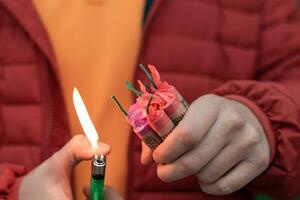 hombre en rojo secuestrado Encendiendo arriba varios petardos en su mano utilizando gas encendedor. chico consiguiendo Listo para nuevo año divertido con fuegos artificiales o pirotécnico productos foto