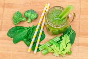 Fresco verde zalamero de manzana, apio, y Espinacas en vaso zalamero tarro con amarillo cóctel Paja en de madera corte tablero. vegano desintoxicación beber. vegetariano cultura. sano comiendo y Fruta dieta foto