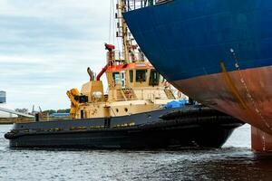 Tug ship towing blue bulk carrier in the port of Riga photo