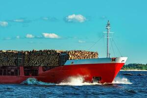 Red cargo ship fully loaded with wood moving at clear day photo
