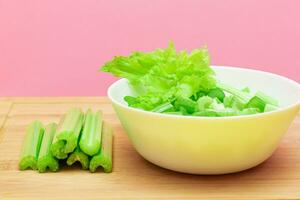 Fresh Chopped Celery Slices in White Bowl with Celery Sticks on Bamboo Cutting Board. Vegan and Vegetarian Culture. Raw Food. Healthy Diet with Negative Calorie Content photo