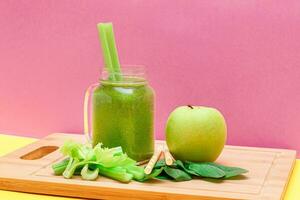 Fresco verde zalamero de manzana, apio, y Espinacas en vaso zalamero tarro con amarillo cóctel Paja en de madera corte tablero. vegano desintoxicación beber. vegetariano cultura. sano comiendo y Fruta dieta foto