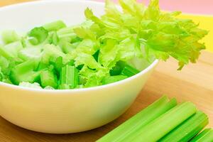 Fresh Chopped Celery Slices in White Bowl with Celery Sticks on Bamboo Cutting Board. Vegan and Vegetarian Culture. Raw Food. Healthy Diet with Negative Calorie Content photo