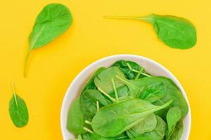 Fresh Baby Spinach Leaves in White Bowl on Yellow Background Top View. Vegan and Vegetarian Culture. Raw Food, Green Leaves. Healthy Diet photo