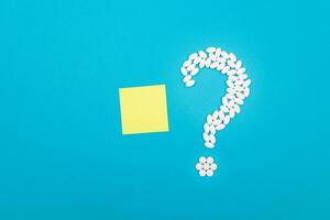 Question Mark Made from White Pills and Tablets with Small Blank Memo Paper, Lying on Blue Background. Global Pharmaceutical Industry and Medicinal Products photo