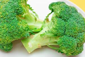 Two Fresh and Raw Pieces of Broccoli on White Plate. Uncooked Green Cabbage. Vegan and Vegetarian Culture. Raw Food. Healthy Eating and Vegetable Diet photo