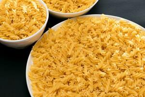 Uncooked Fusilli Pasta Lying on White Plate on Black Background. Raw and Dry Macaroni. Unhealthy and Fat Food photo
