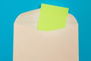 Beige Envelope with Blank Green Sheet of Paper Inside, Lying on Blue Background Mock Up with Copy Space. Receiving Mail or Notice, Sending Postcard Top View, Flat Lay photo