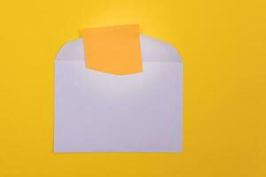 Violet Envelope with Blank Orange Sheet of Paper Inside, Lying on Yellow Background Mock Up with Copy Space. Receiving Mail or Notice, Sending Postcard Top View, Flat Lay photo