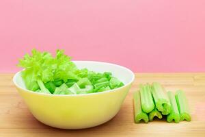 Fresh Chopped Celery Slices in White Bowl with Celery Sticks on Bamboo Cutting Board. Vegan and Vegetarian Culture. Raw Food. Healthy Diet with Negative Calorie Content photo