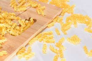 Uncooked Fusilli Pasta Scattered on Wooden Board and White Table. Raw and Dry Macaroni. Fat and Unhealthy Food photo