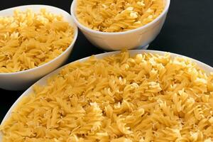 Uncooked Fusilli Pasta Lying on White Plate on Black Background. Raw and Dry Macaroni. Unhealthy and Fat Food photo