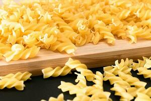 Uncooked Fusilli Pasta Scattered on Wooden Board and Black Table. Raw and Dry Macaroni. Fat and Unhealthy Food photo