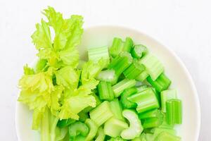 Fresh Chopped Celery Slices with Water Drops on White Dish Top View. Vegan and Vegetarian Culture. Raw Food. Healthy Diet with Negative Calorie Content photo