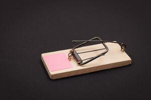 Blank Pink Sheet of Paper in Wooden Mousetrap Template. Small Memo Paper in Mouse Trap on Black Background photo