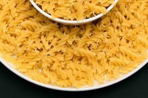 Uncooked Fusilli Pasta Lying on White Plate on Black Background. Raw and Dry Macaroni. Unhealthy and Fat Food Top View photo