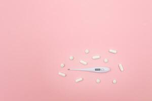 White Pills or Tablets with Electronic Thermometer on Pink Background. Pharmaceutical Industry and Medicinal Products photo