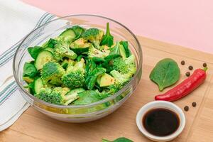 Fresh Green Salad of Avocado, Broccoli, Spinach and Cucumber with Soy Sauce and Red Hot Pepper on Wooden Cutting Board. Vegan Salad. Vegetarian Culture. Raw Food. Healthy Eating and Vegetable Diet photo