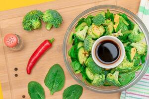 Fresh Green Salad of Avocado, Broccoli, Spinach and Cucumber with Soy Sauce and Red Hot Pepper on Wooden Cutting Board. Vegan Salad. Vegetarian Culture. Raw Food. Healthy Eating and Vegetable Diet photo