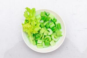 Fresh Chopped Celery Slices with Water Drops on White Dish Top View. Vegan and Vegetarian Culture. Raw Food. Healthy Diet with Negative Calorie Content photo