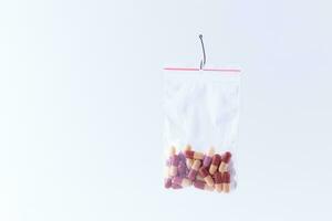 The Pharmaceutical Trap and Drug Addiction Colored Pills or Tablets Hanging in Small Ziplock Bag on a Fishing Hook Against the White Background photo