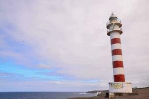 un faro en el costa con un rojo y blanco a rayas torre foto