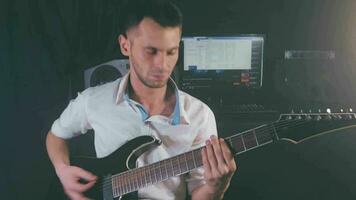 Medium CloseUp Shot of a Handsome Young Man Playing Electric Guitar in a Dark Smoky Room. Active Emotional Musician in a White Shirt is Recordind Music at the Home Studio Against the Black Background video