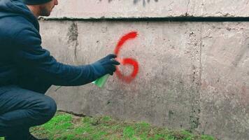 jung Mann vandalisiert das Mauer. Rowdy ist Schreiben ein gut Wort mit ein rot sprühen malen. Graffiti Gemälde draußen. Jugend Bewegung Verbrechen verbunden mit Straße Kunst. Rückseite Sicht, dynamisch Schuss video