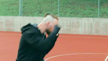 jovem barbudo caucasiano branco cara 20s dentro casual Preto roupas e ataduras em a pulso praticando boxe socos ao ar livre às a estádio. masculino boxer comovente punhos dentro lento movimento video