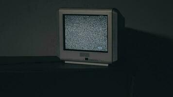bruten tv gammal silver- TV på svart tabell i mörk rum. Sök för signal. förvrängning på de skärm. närbild, statisk skott, filma spannmål video