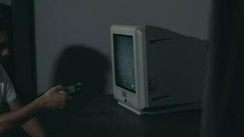 quebrado televisão ou televisão propaganda. mente ao controle zumbificado homem dentro branco camiseta comuta canais em a velho televisão dentro Sombrio sala. televisão sinal procurar. distorção em a tela. médio fechar-se, filme grão video