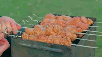 man är matlagning fläsk utomhus och vändning utegrill kött på spett. varm grillad kebab på de kol. picknick mat förbereder. mitten närbild skott video