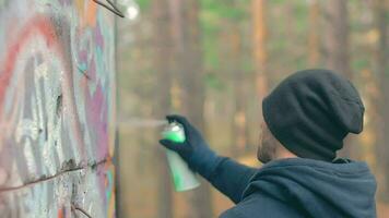 jovem cara vandaliza a parede usando uma spray pintura pode. vândalo dentro casual roupas é desenhando grafite ao ar livre. juventude movimento crime relacionado com rua arte. meio fechar-se visualizar, dinâmico tiro video