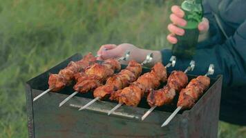 Mann ist Kochen Schweinefleisch Fleisch draußen, halten Bier im Grün Flasche und drehen Grill auf Spieße. heiß gegrillt Kebab auf das Kohlen. Picknick Essen vorbereiten. Mitte Nahansicht Schuss video