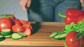 femme dans bleu jeans est Coupe des légumes à maison. femme au foyer est en train de préparer Ingrédients pour quelque chose diététique. en bonne santé nourriture concept. statique fermer coup video