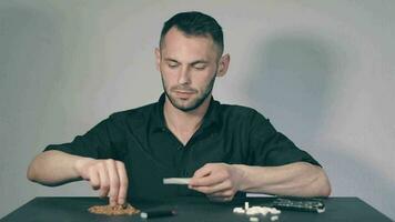 Man in Black Clothing is Rolling a Hand Made Cigarette Using Papers, Filters and Tobacco. A Way to Save on Tobacco Products. Tobacco Product Economy Concept. Middle Angle VIew, Static Shot video