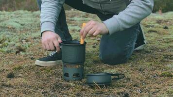 hombre en un bosque es Cocinando pasta con Enlatado estofado utilizando un pequeño cocinar colocar. turista en un caminata es preparando para el almuerzo. de cerca vista, estático Disparo video