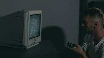 quebrado televisão ou televisão propaganda. mente ao controle zumbificado homem dentro branco camiseta comuta canais em a velho televisão dentro Sombrio sala. televisão sinal procurar. distorção em a tela. médio fechar-se, filme grão video