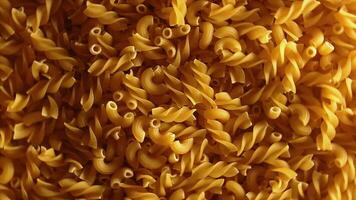 ongekookt fusilli en chifferi rigati pasta top visie, laag sleutel licht. dik en ongezond voedsel. klassiek droog macaroni, roterend achtergrond. rauw verschillend macaroni pasta structuur draaien links video