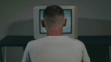 rotto televisione o tv propaganda zombificato uomo nel bianca maglietta è seduta contro il vecchio argento tv nel buio camera. ricerca per tv segnale. distorsione su schermo. indietro Visualizza, statico sparo, film grano video