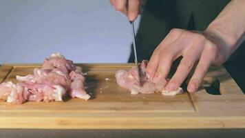 capocuoco nel nero uniforme è taglio pollo filetto. macellaio è preparazione cibo ingredienti per cucinando lento movimento. statico tiro video