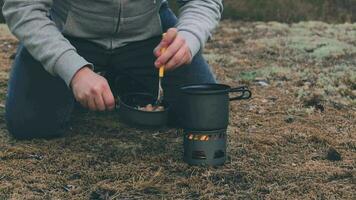 Mens in een wandeltocht is Koken pasta met ingeblikt tonijn gebruik makend van een klein koken set. toerist in een wandeltocht is voorbereidingen treffen voor de avondeten in avond. statisch detailopname schot video